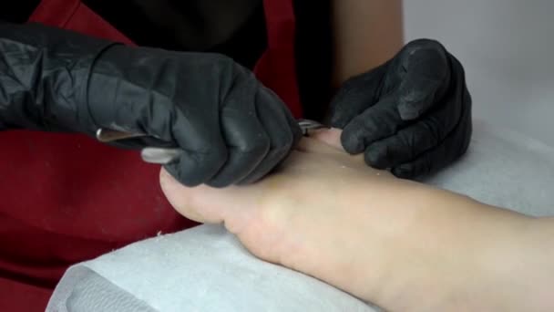 Мастер педикюр в черных перчатках удаляет избыток кожи, ногти на ногтях ножницами — стоковое видео