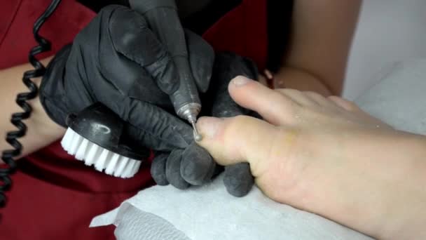 Maître pédicure en tablier rouge travaille un routeur sur les ongles des filles à pied — Video