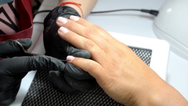 Мастер маникюра в перчатках режет кутикулу с пальца клиента тонкими ножницами — стоковое видео