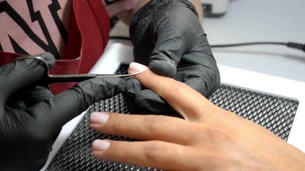 Манікюр майстер в рукавичках вирізає кутикулу з клієнтського пальця з тонкими ножицями — стокове відео