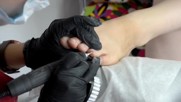 Мастер педикюра в фартуках и черных перчатках работает с маршрутизатором с мельницей, на пальцах ног — стоковое видео