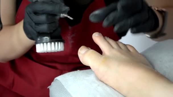 Pediküre-Meister in roter Schürze und Handschuhen arbeitet mit Router mit Fräse, an Mädchenzehe — Stockvideo