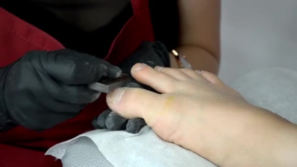 Pedicure master en tablier rouge et gants noirs fonctionne avec lime à ongles sur les orteils de fille — Video