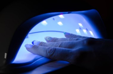 Woman hand lies in an ultraviolet lamp with blue shining in dark room clipart