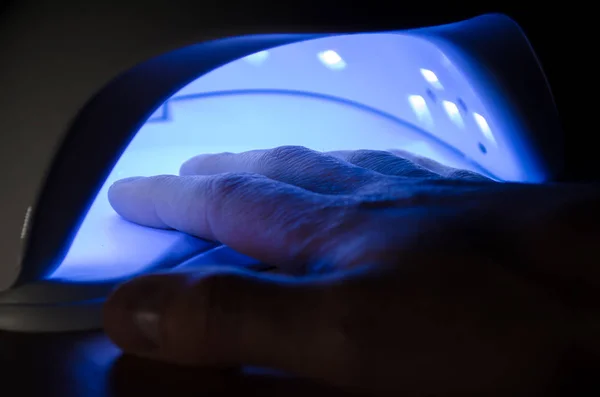Το ανθρώπινο χέρι βρίσκεται σε μια υπεριώδη λάμπα με μπλε λάμψη στο σκοτεινό δωμάτιο — Φωτογραφία Αρχείου