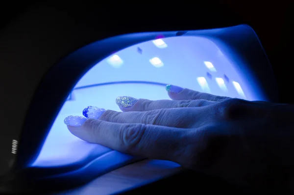 Mujer mano se encuentra en una lámpara ultravioleta con azul brillante en habitación oscura — Foto de Stock