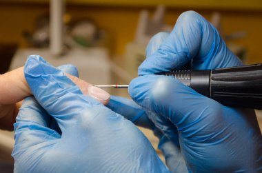 Donanım manikür prosedürü. Mavi eldivenli usta çiviyi uzun bir değirmenle manikür yapar, hizalar ve çivileri temizler.