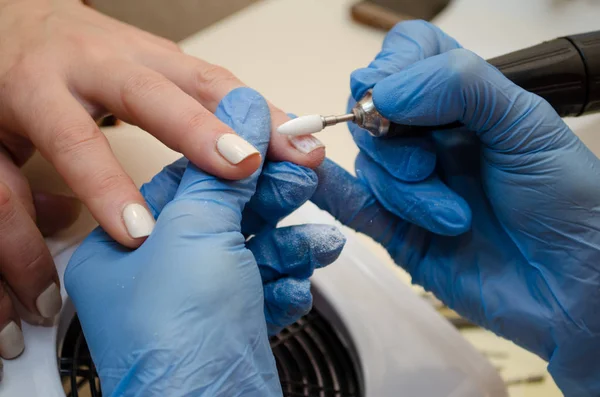 Hardware manicure procedure. Master in blauwe handschoenen verwijdert gel polijsten van nagels met witte cutter — Stockfoto