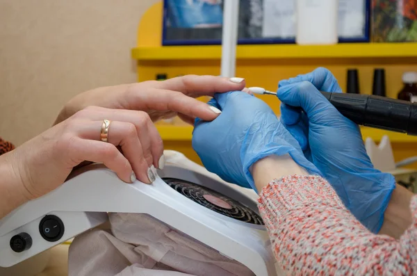 Hardware manicure procedure. Master in blauwe handschoenen verwijdert gel polijsten van nagels met witte cutter — Stockfoto