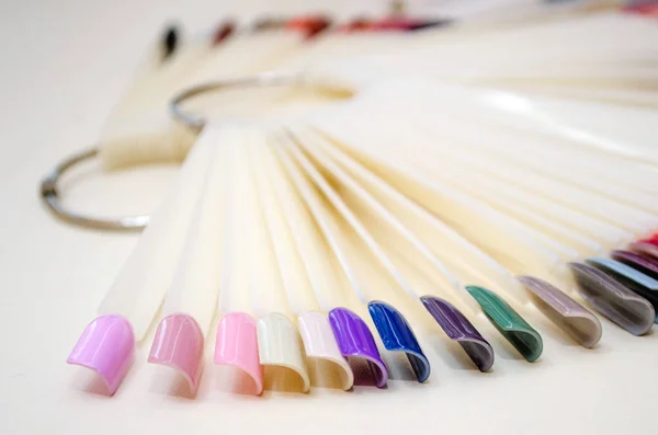 Palette of nail design of different colors with gel polish on white tips and background. Plastic testers for nail polish