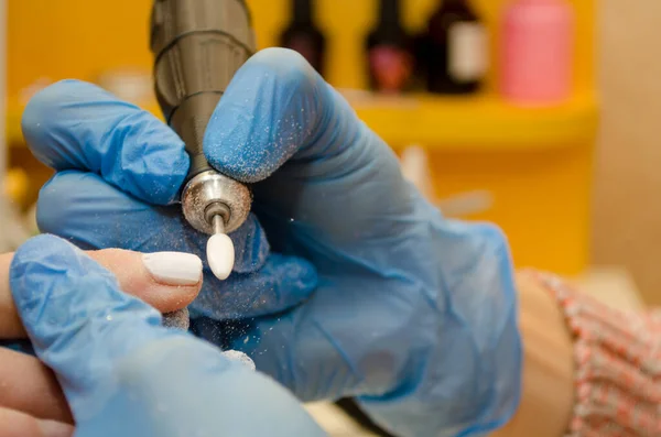 Procedimento de manicure de hardware. Mestre em luvas azuis remove gel polonês de unhas com um cortador branco, moscas de poeira — Fotografia de Stock