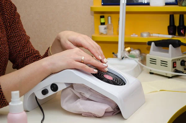 Manikür prosedürü. Müşteri oturuma hazırlanıyor ve ellerini kaputa koyuyor.