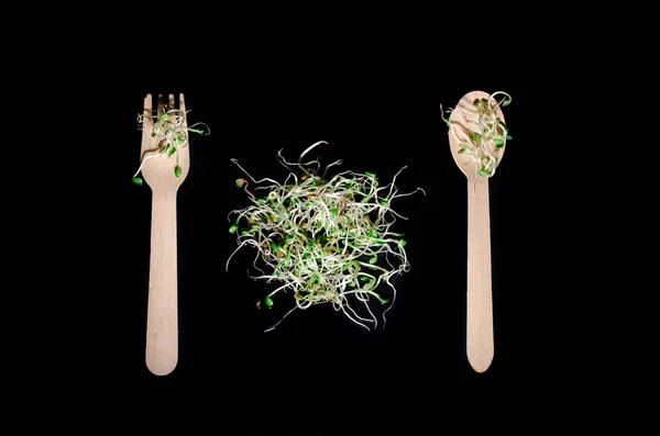 Ramo redondo de brotes microverdes jóvenes sobre un fondo negro, vista superior con cuchara y tenedor — Foto de Stock
