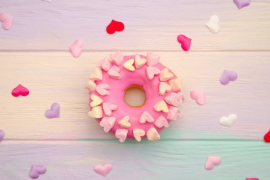 Tatlı pembe çörek ve süsleme ile gökkuşağı ahşap arka planda kalpleri ve dekoratif kalpleri ile