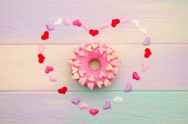 Tatlı pembe donut ve süsleme ile gökkuşağı ahşap arka planda kalpleri ile dekoratif kalp ile