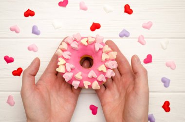 Tatlı pembe donut, kremalı ve süslemeli, kalpler beyaz tahta arka planda, erkeklerin ellerinde.