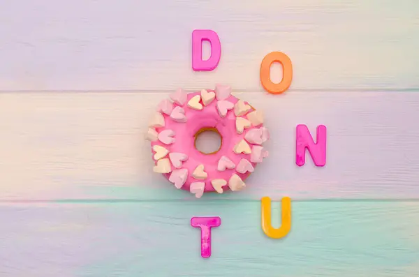 Γλυκό ροζ ντόνατ με κερασάκι και διακόσμηση με καρδιές σε ξύλινο φόντο ουράνιο τόξο και με γράμματα κειμένου — Φωτογραφία Αρχείου