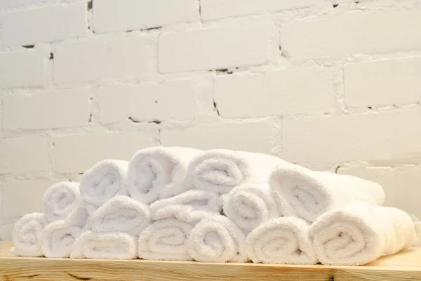 White terry towels, rolled up in rolls, lie on wooden table against a brick wall in a barbershop for men — Stock Photo, Image