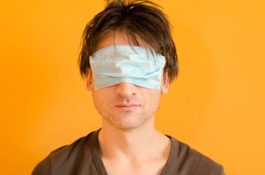 Gözlerinde maske olan yorgun bir adam, onu virüsten değil, sarı arka planda, maskeyi yanlış takmış.