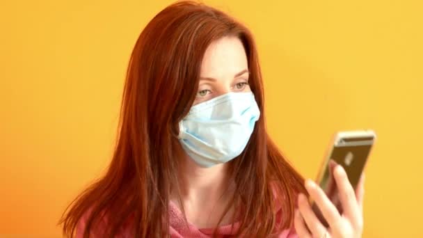 Flicka i medicinsk mask talar på mobiltelefon, gul vägg, epidemi av coronovirus — Stockvideo