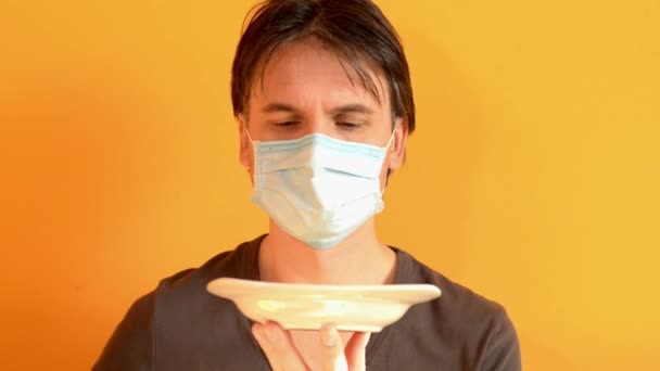 男は皿からスプーンで食べ物を食べるしようとし、彼は医療マスクでそれを行うことはできません — ストック動画