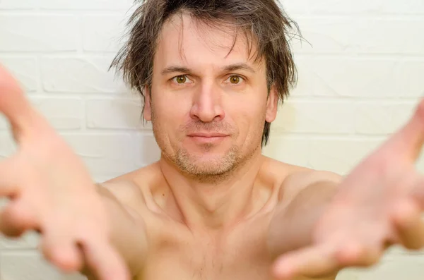 Emotional crazy man with bristles and shaggy hair, on white brick background pulls hands into frame, inviting somewhere — Stock Photo, Image