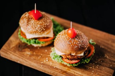 Two mouth-watering delicious homemade burger used to chop beef. on the wooden table. The burgers are inserted knives. clipart