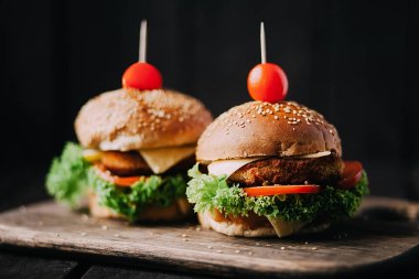 Two mouth-watering delicious homemade burger used to chop beef. on the wooden table. The burgers are inserted knives. clipart