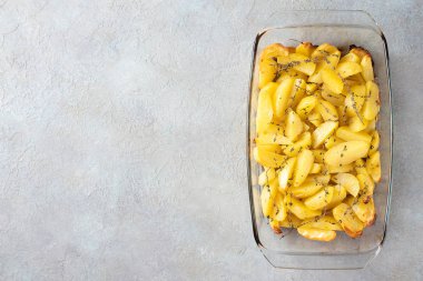 Fırında patates, zeytinyağı, sarımsak ve kekik hafif desenli arka planda cam bir formda. Düz yatış, üst görünüm.