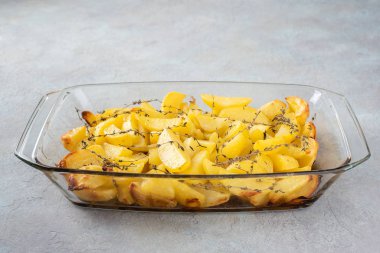 Fırında patates, zeytinyağı, sarımsak ve kekik hafif desenli arka planda cam bir formda..