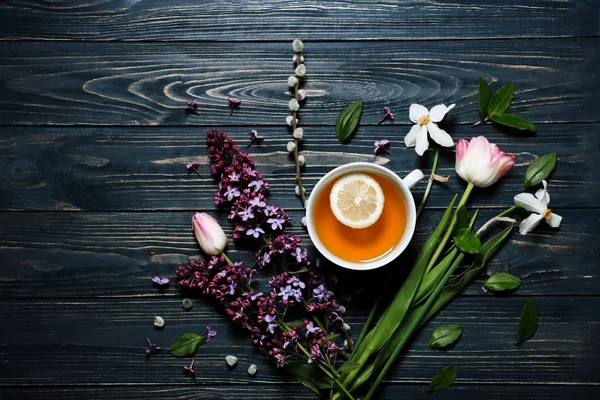 Creative design of flowers.Flat lay underground style. A cup of tea with lemon with spring flowers on dark background view from above. Place for text.