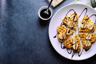 Çikolata sosu ve koyu gri arka plan üzerinde muz ile tabak Belçikalı waffle. Üstten Görünüm