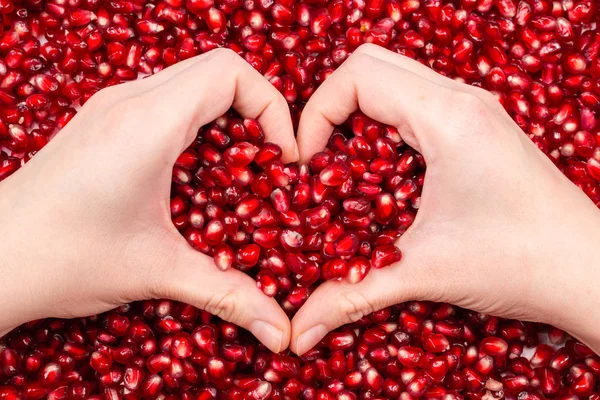 Símbolo del corazón. Semillas de granada en mano de mujer . — Foto de Stock