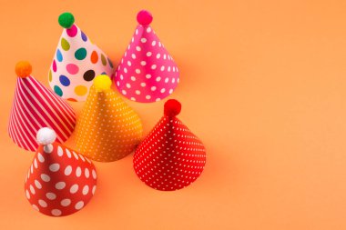 Turuncu arkaplanda renkli doğum günü şapkaları.