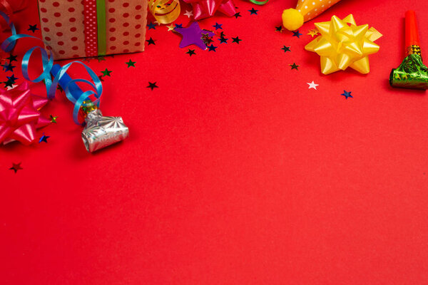 Праздничные золотые и фиолетовые звезды конфетти и подарок, шляпы на красном фоне. Пространство для текста или дизайна
.