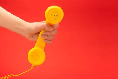Kadın elinin kırmızı arka planında sarı bir cep telefonu. Boşluğu kopyala.