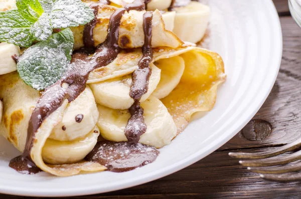 French crepes with chocolate sauce and banana in ceramic dish on