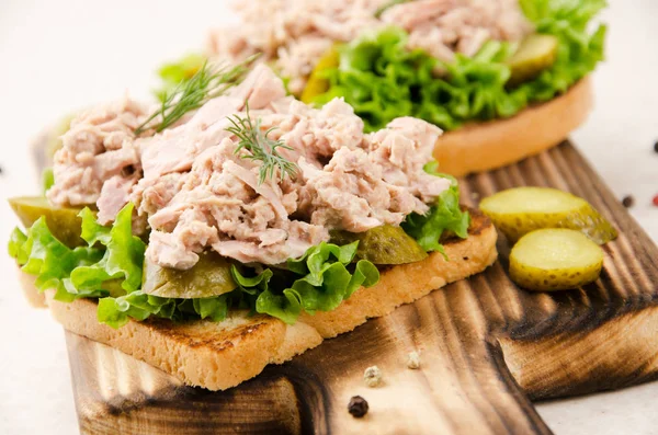 Homemade tuna salad sandwiches on cutting board with pickles asi