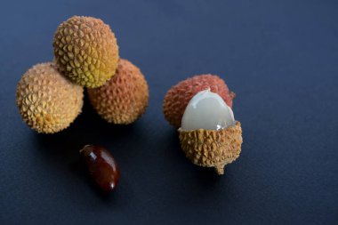 Lychee (Litchi)  with a stone and bright, bumpy skin on dark blue (black) background  clipart