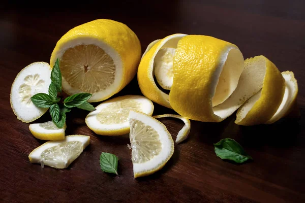 Lemon peel or lemon twist on a dark brown wooden background with a sprig of fragrant, green mint. Lemon slices are cut across. Close up. Citrus limon. Mentha.