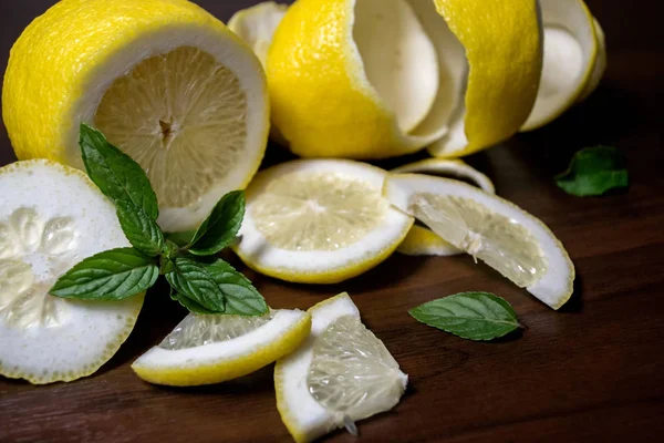 Lemon peel or lemon twist on a dark brown wooden background with a sprig of fragrant, green mint. Lemon slices are cut across. Close up. Citrus limon. Mentha.