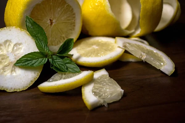 Lemon peel or lemon twist on a dark brown wooden background with a sprig of fragrant, green mint. Lemon slices are cut across. Close up. Citrus limon. Mentha.