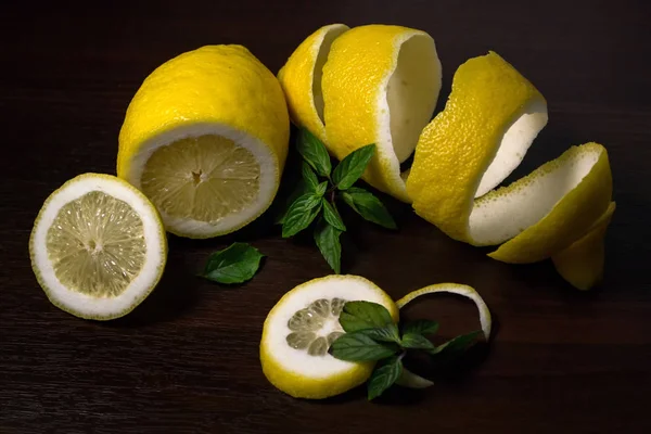 Lemon peel or lemon twist on a dark brown wooden background with a sprig of fragrant, green mint. Lemon slices are cut across. Close up. Top view. Citrus limon. Mentha.