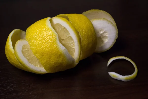 Lemon peel or lemon twist on a dark brown wooden background. Lemon slices are cut across. Close up. Citrus limon.