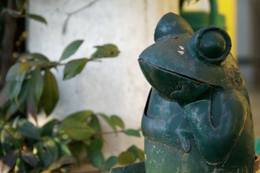 Çelik yeşil kurbağa taş merdivenlerde çapraz bacak hareketi oturur. Bahçe heykeli Kurbağa yüzüne seçici odak.