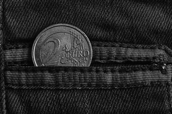 Monochrome Euro coin with a denomination of 2 euro in the pocket of warn blue denim jeans with red laces