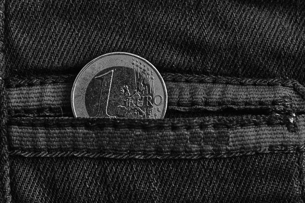 Monochrome Euro coin with a denomination of 1 euro in the pocket of worn blue denim jeans with red laces