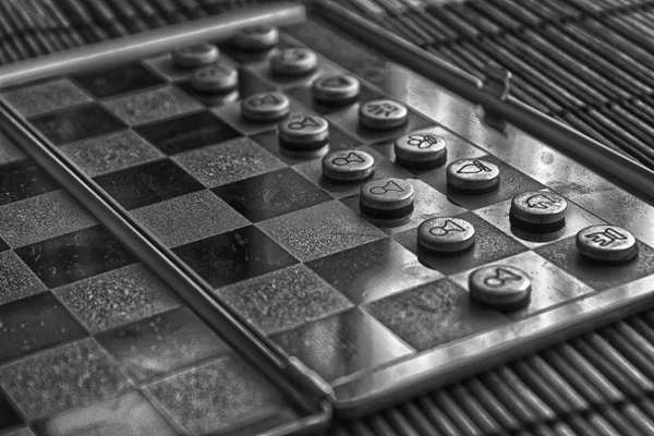 Foto monocromática com uma foto de um tabuleiro de aço de xadrez e peças de xadrez, peças de xadrez de metal em um tabuleiro de xadrez com reflexão — Fotografia de Stock