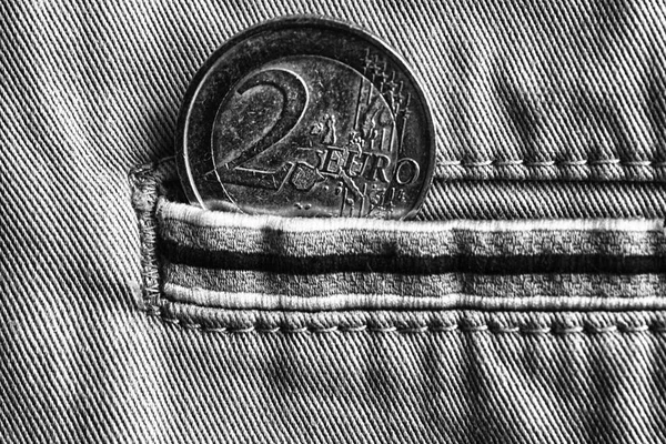 Euro coin with a denomination of 2 euro in the pocket of denim jeans with stripe, monochrome shot