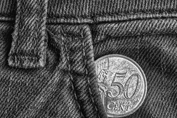 Euro coin with a denomination of 50 euro cents in the pocket of old denim jeans, monochrome shot